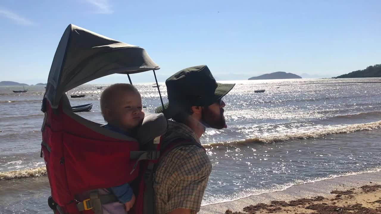 爸爸背着可爱的小女儿在海滩徒步旅行背包视频下载