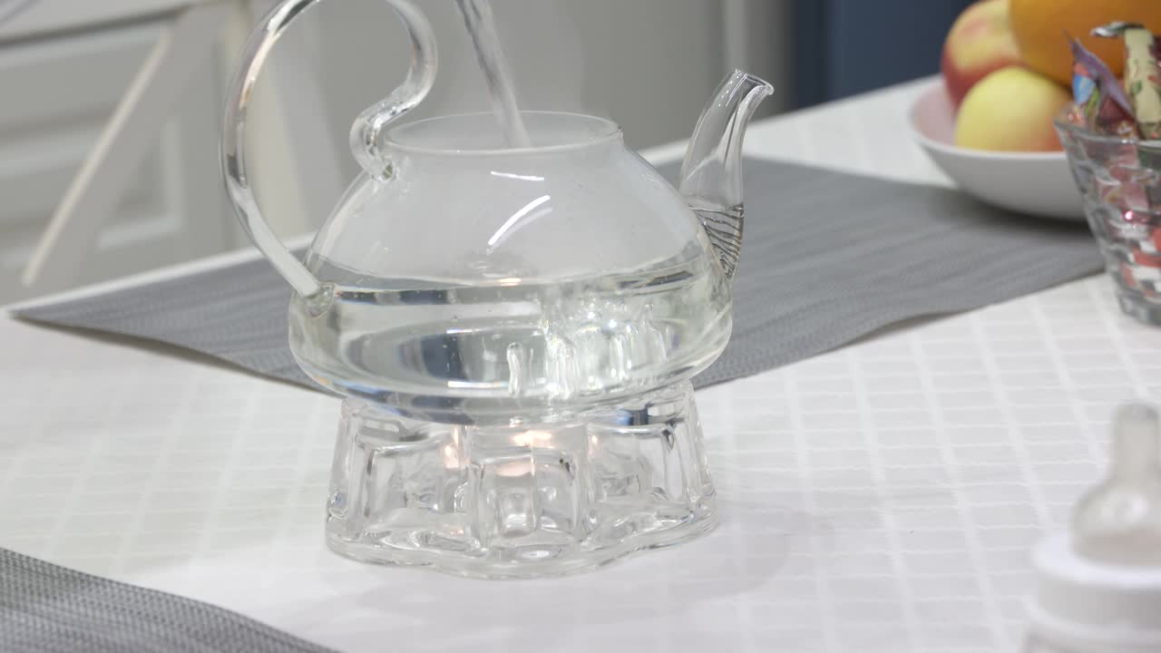 在暖炉上用玻璃茶壶泡茶，点燃茶蜡烛，在厨房的茶壶里倒开水。早餐时间。视频下载