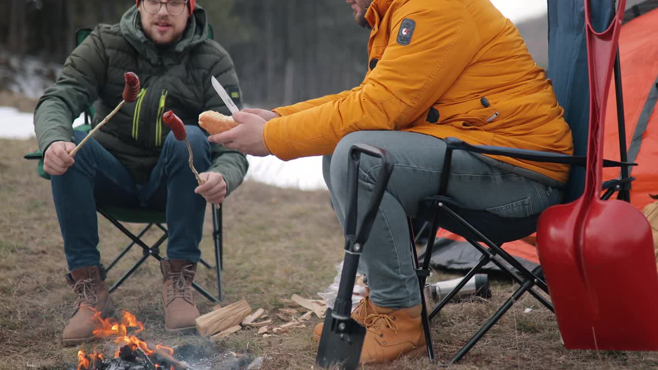 两个男人围坐在森林里的营火旁烤香肠视频下载
