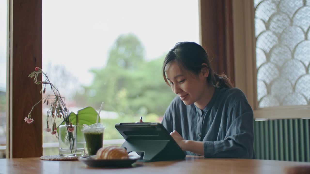 一名亚洲女性在咖啡店使用电子平板电脑视频下载