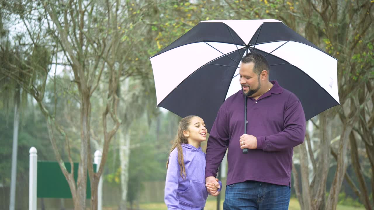 西班牙女孩，父亲在雨天撑着伞散步视频素材