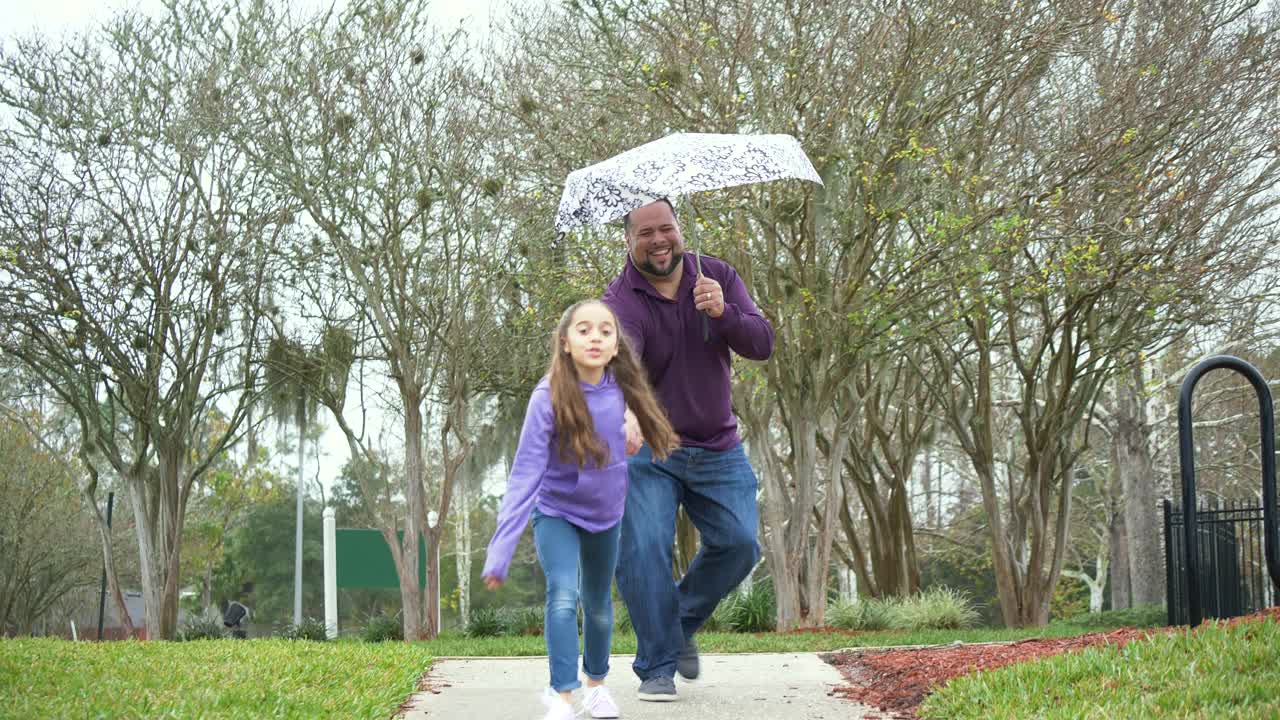 西班牙女孩和父亲打着伞在雨中奔跑视频素材