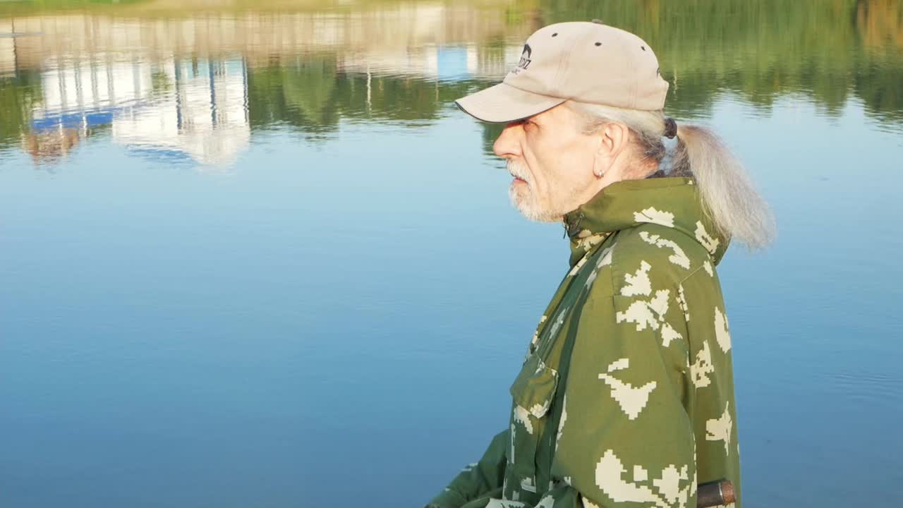 河岸边老大，一个人拿着钓竿钓鱼，美丽的大自然，秋天。一位老人休息并热爱他的爱好。积极健康的生活方式，户外运动。特写肖像视频下载