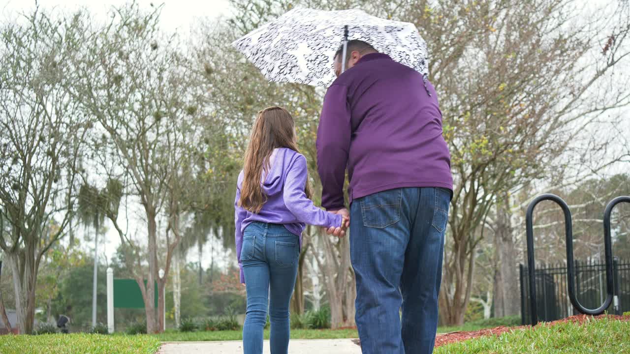 西班牙女孩和父亲撑着伞在雨中行走视频素材