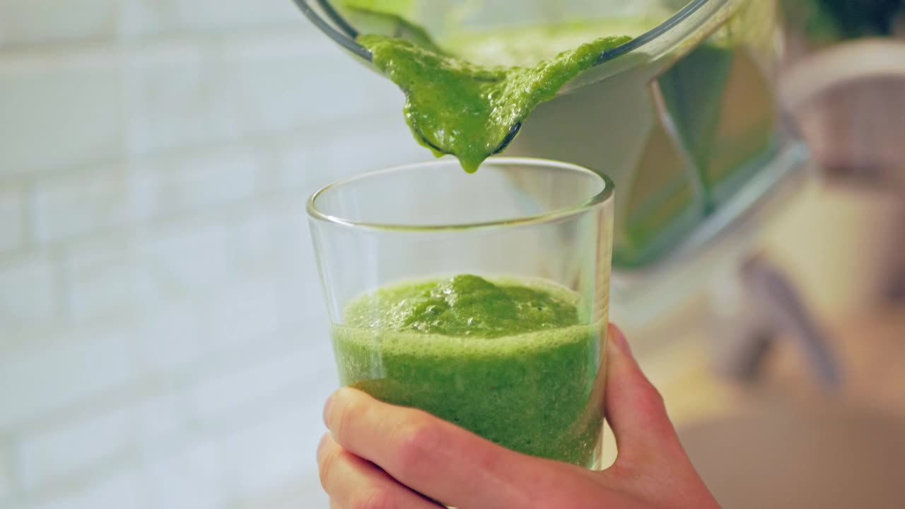 特写镜头中，女人们拿着搅拌机和盛有绿色冰沙的玻璃杯。健康饮食的概念，生食饮食视频素材