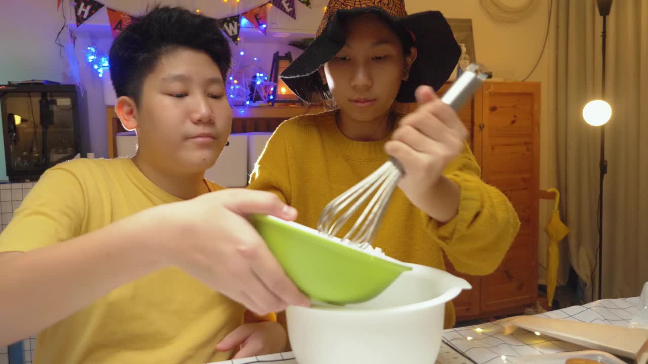 亚洲女孩戴着女巫的帽子，晚上和哥哥一起在家做糖霜饼干，万圣节的生活理念。视频下载