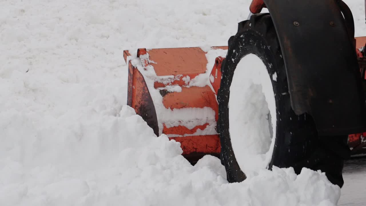 冬天，一辆带着黄色铲斗的拖拉机在街上铲雪。道路清扫援助。慢动作视频下载