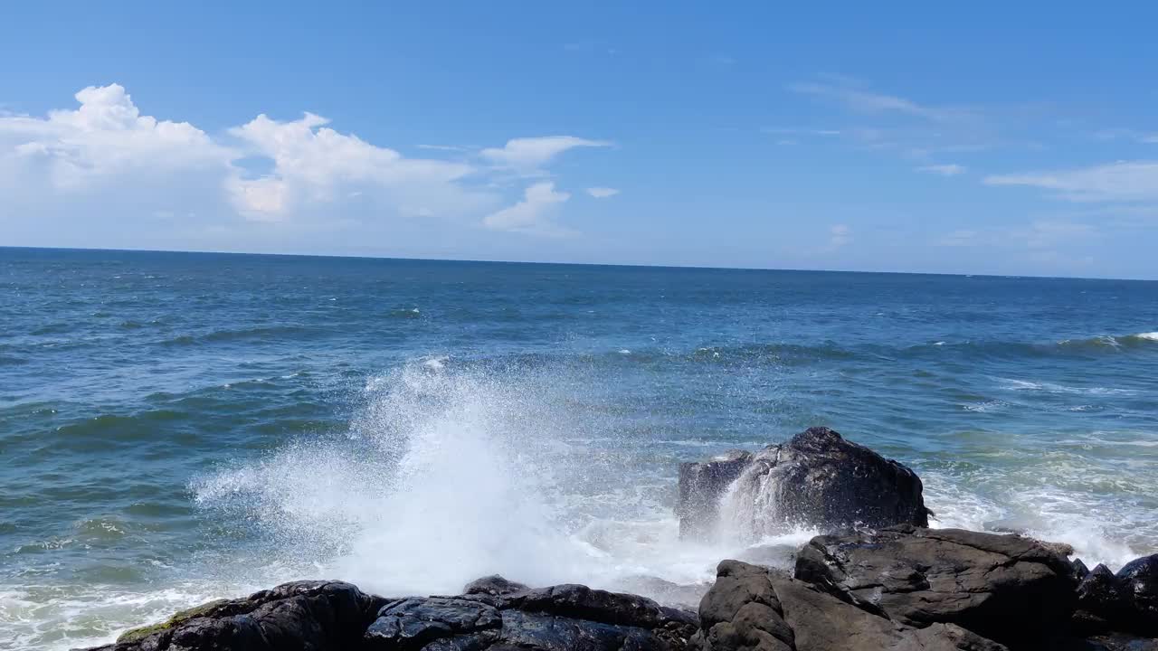 在阳光明媚的日子里，蔚蓝的天空下，海浪拍打着海边的岩石，令人惊叹视频下载
