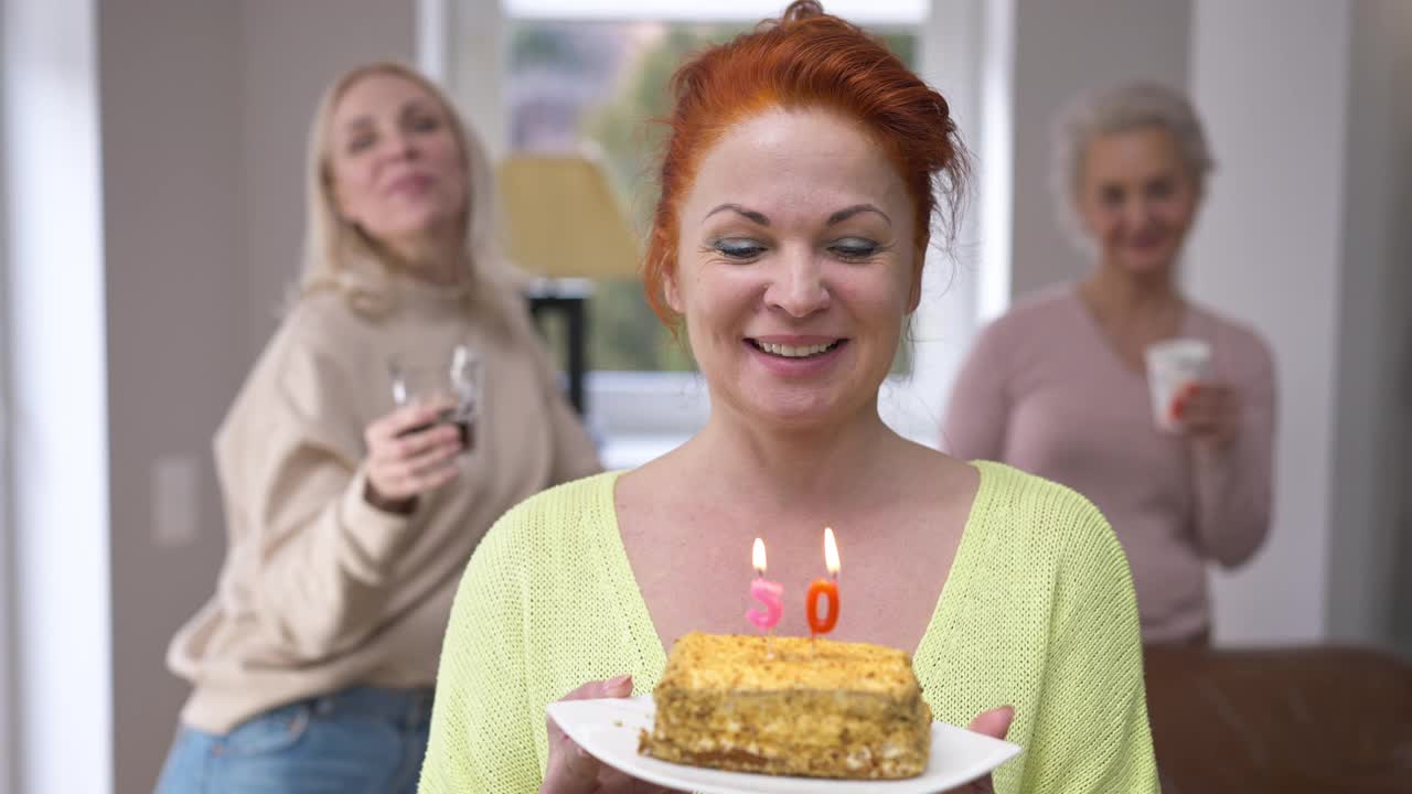 正面快乐的女人吹蜡烛蛋糕许愿看着镜头微笑。激动美丽的白人女士的肖像庆祝50岁生日在家里与朋友摆姿势视频素材