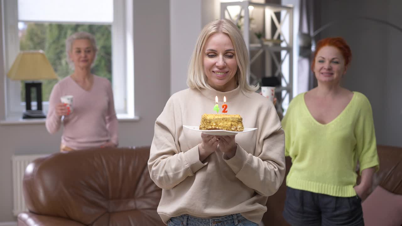42岁生日当天，在生日蛋糕上吹蜡烛的美丽的白人成年女性在朋友的欢呼声中微笑着许愿。快乐的美丽苗条的女士在家里摆姿势度假视频素材