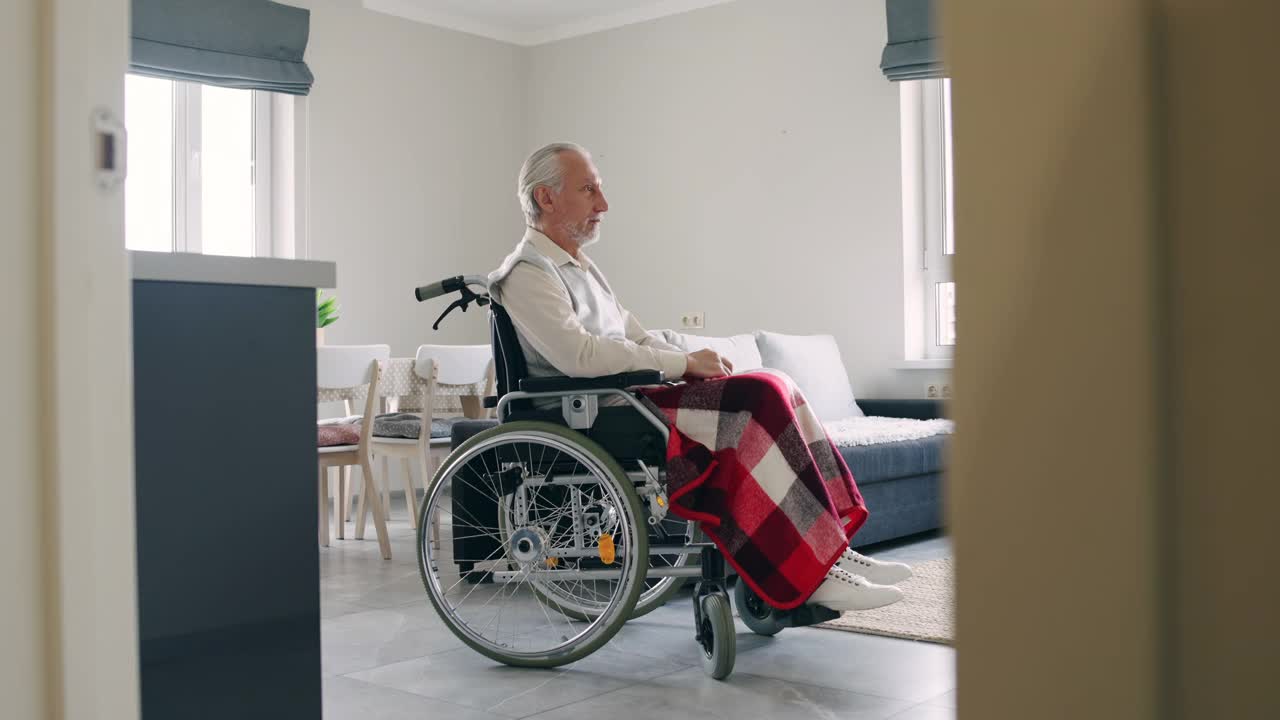 坐在轮椅上独自生活的老人在家里感到悲伤视频素材