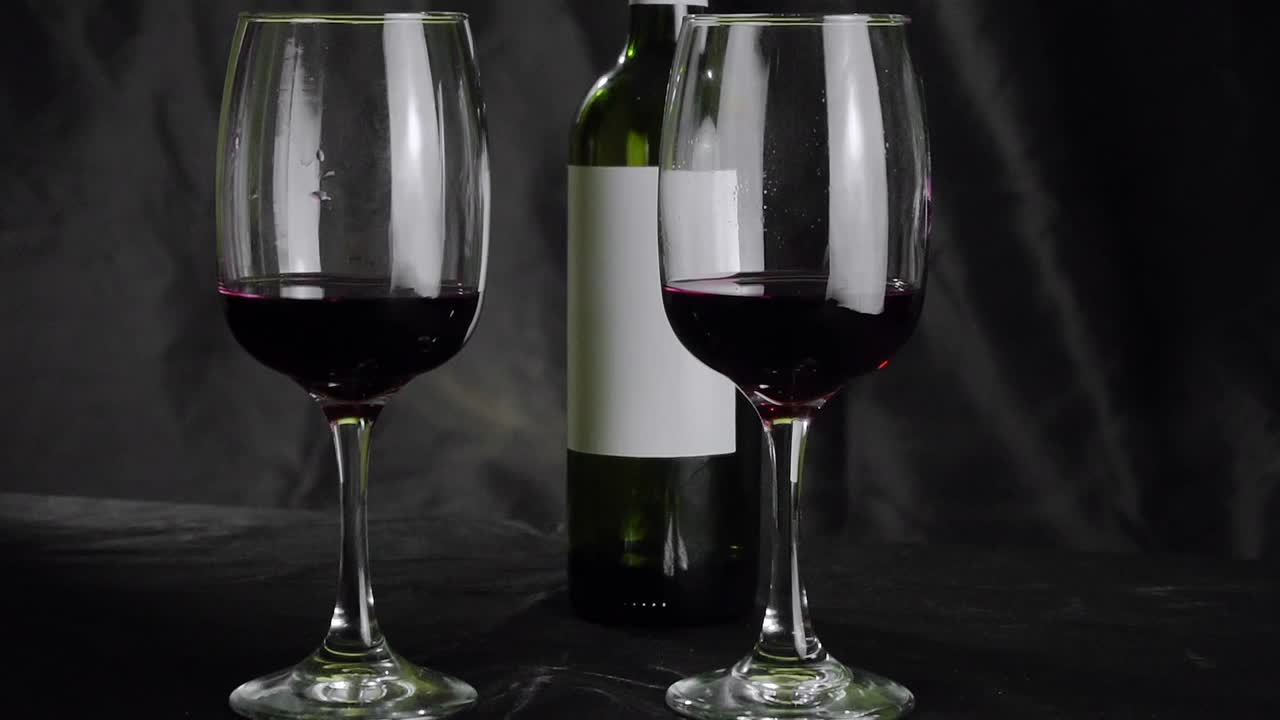 桌子上有两杯红酒和一瓶。黑色背景视频下载