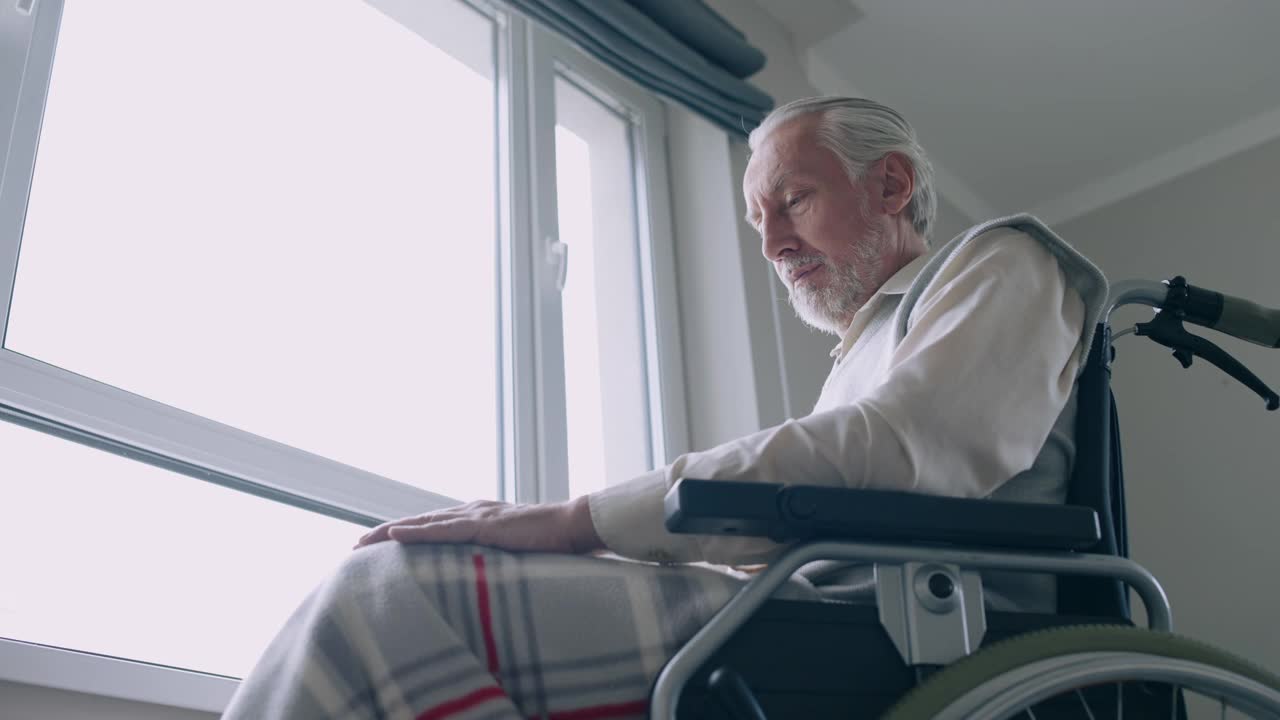 孤独的残疾人老人坐在靠窗的轮椅上视频素材