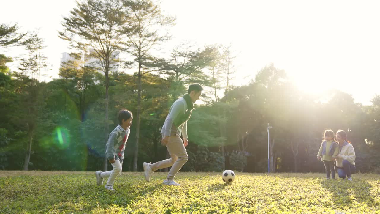 一个亚洲小男孩和爸爸在公园里踢足球视频素材