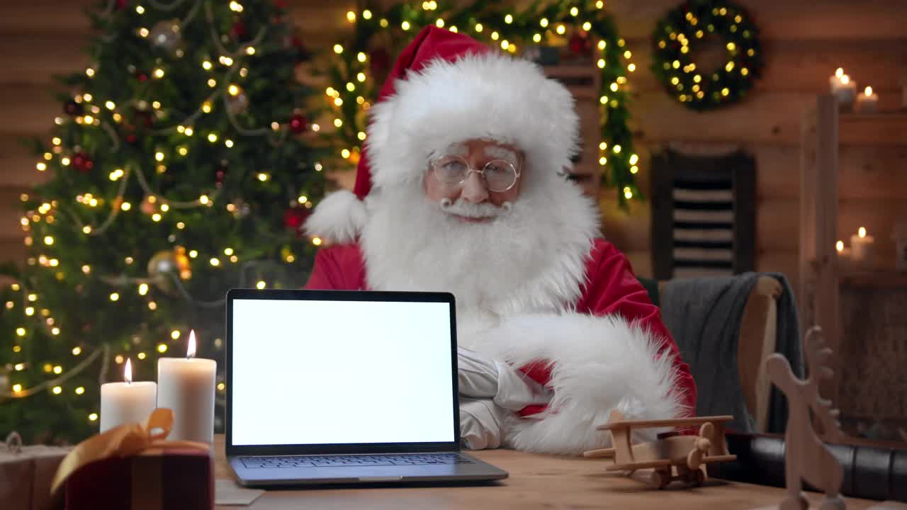 圣诞老人坐在装饰华丽的室内，在镜头前竖起大拇指，他面前是一个空的笔记本电脑屏幕视频素材