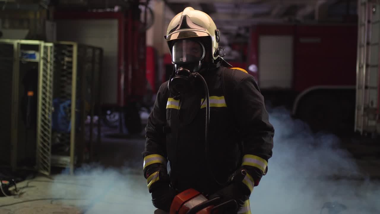 身穿全套装备、氧气面罩、电动液压切割工具的消防员肖像，背景是烟雾和消防车视频素材