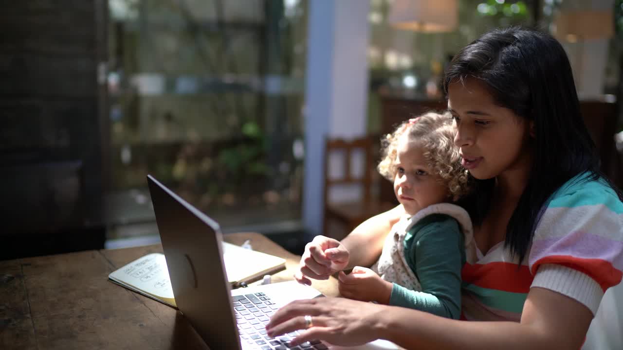 母亲抱着愤怒的女儿在家里用笔记本电脑视频下载