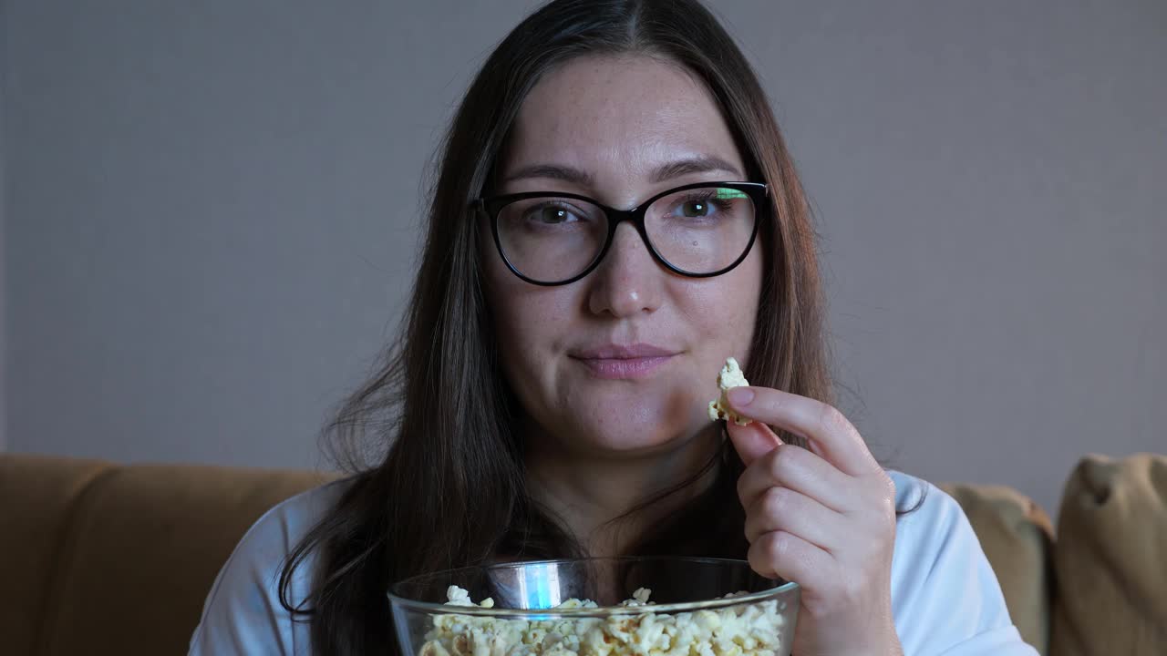 戴眼镜的女人一边吃爆米花一边看电视视频素材