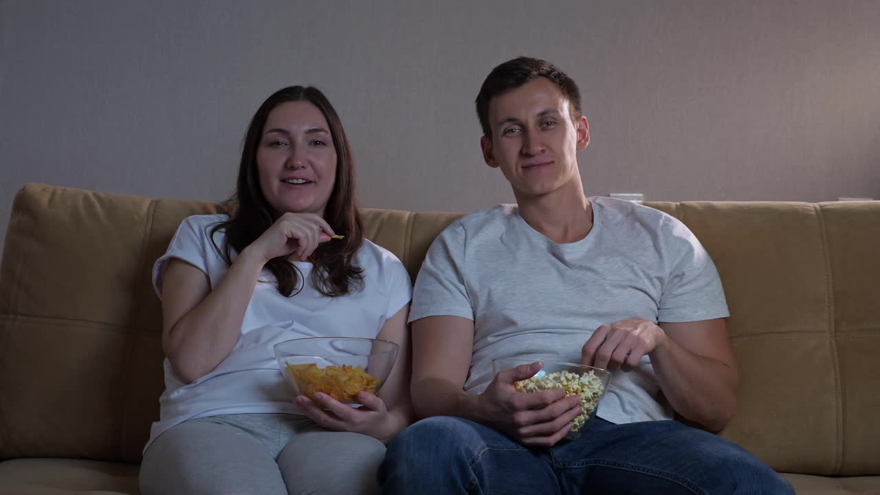 男人拿着爆米花，女人拿着薯条看电视视频素材