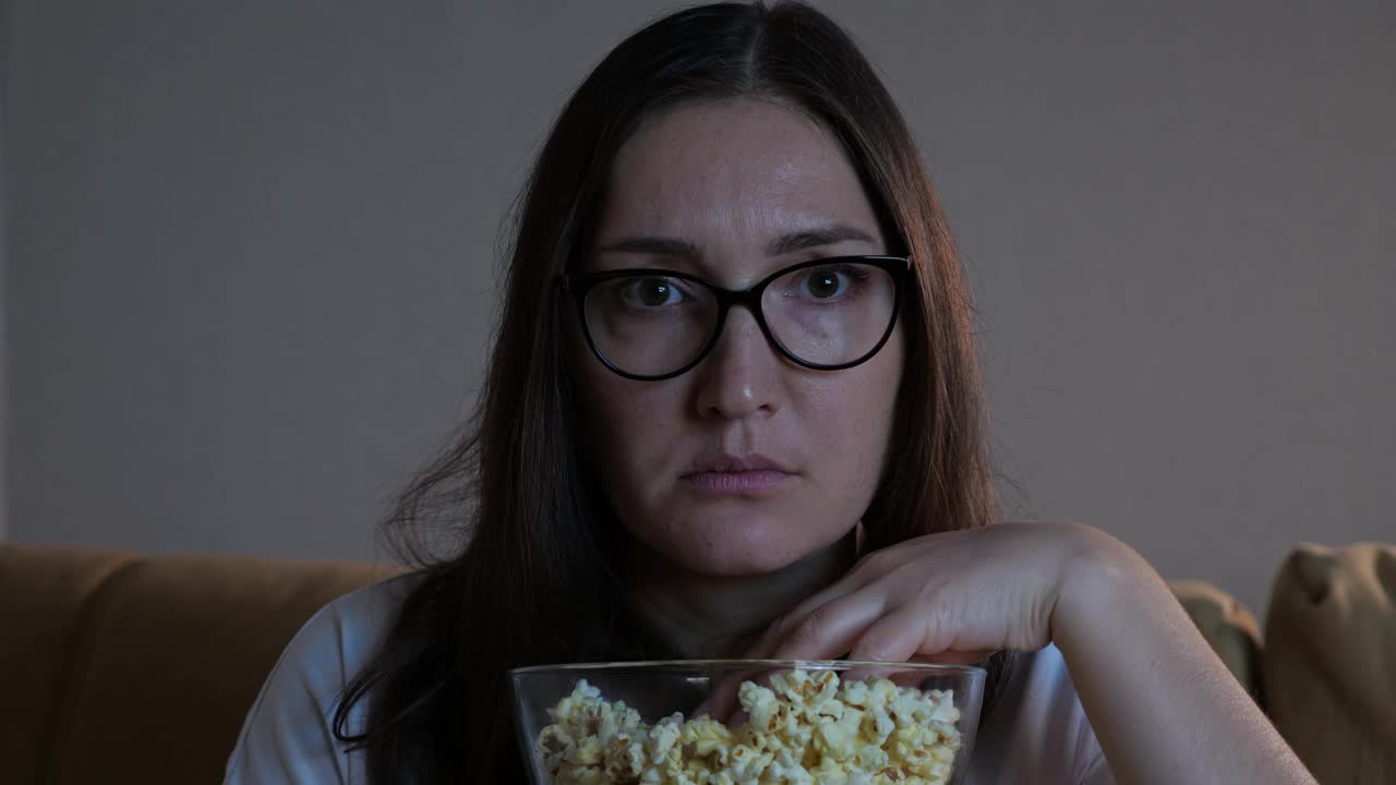 一脸恐惧的女士一边看恐怖电影一边吃爆米花视频素材