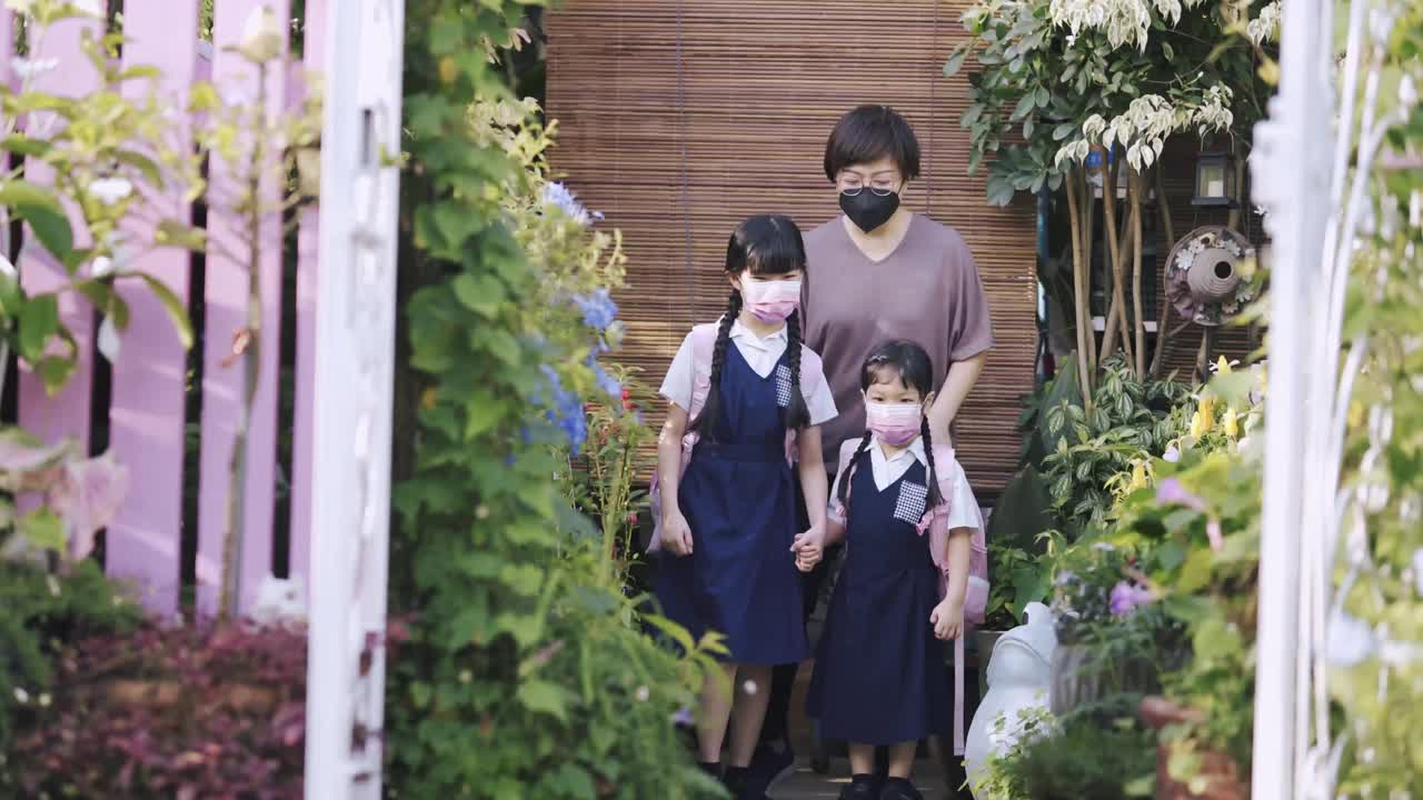 回到学校的亚洲华人母亲送她的两个女儿上学从家在前院的房子防护口罩视频素材