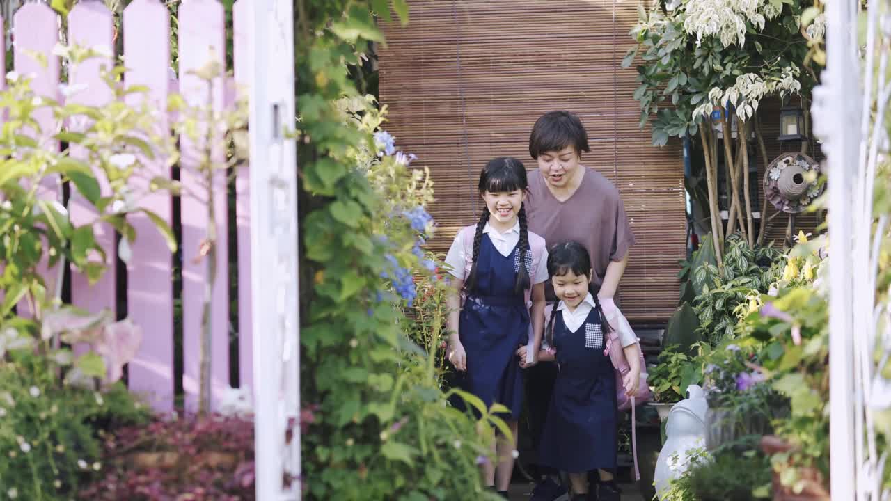 一位亚洲华裔母亲早上把她的两个女儿送到她家的前院上学视频素材