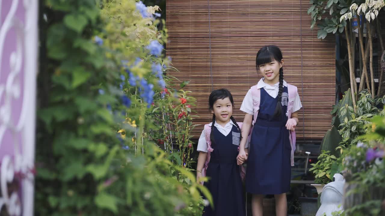 早上，亚洲的中国姐妹们手牵着手从家走到房子的前院上学视频素材