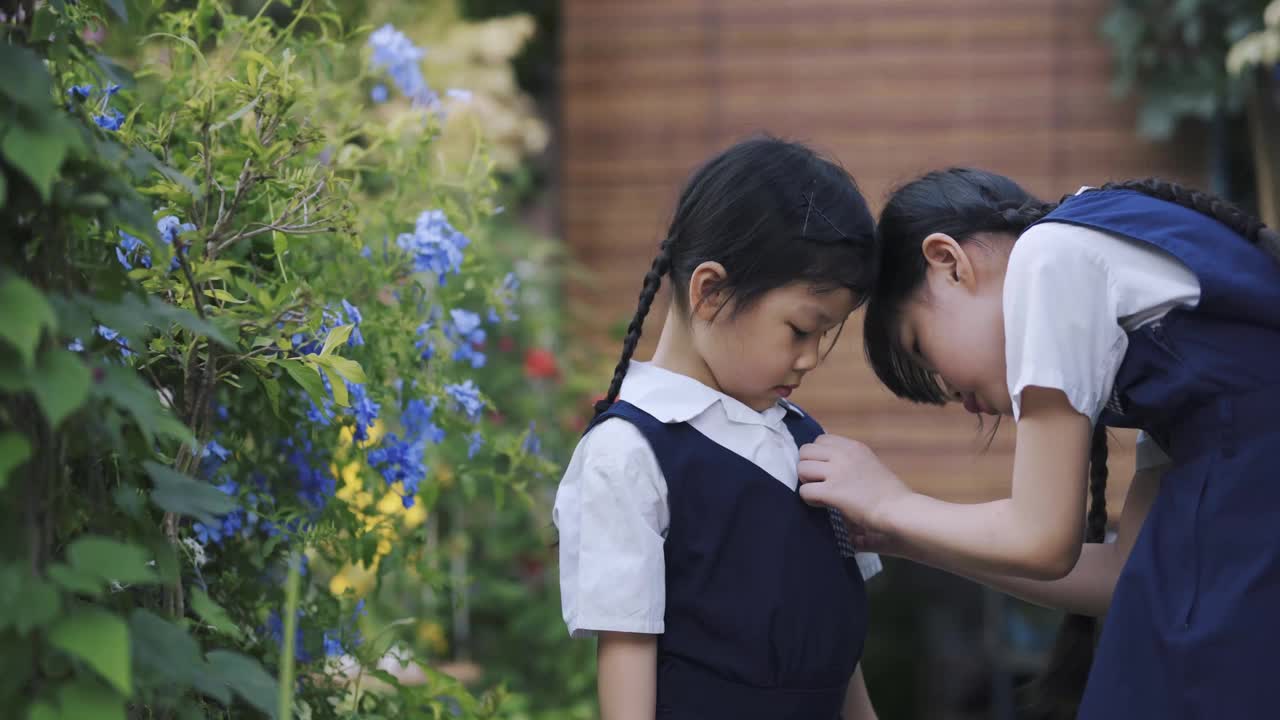 回到学校的亚洲华人姐姐在早上从家到学校的前院里帮妹妹戴上校名标签徽章视频素材