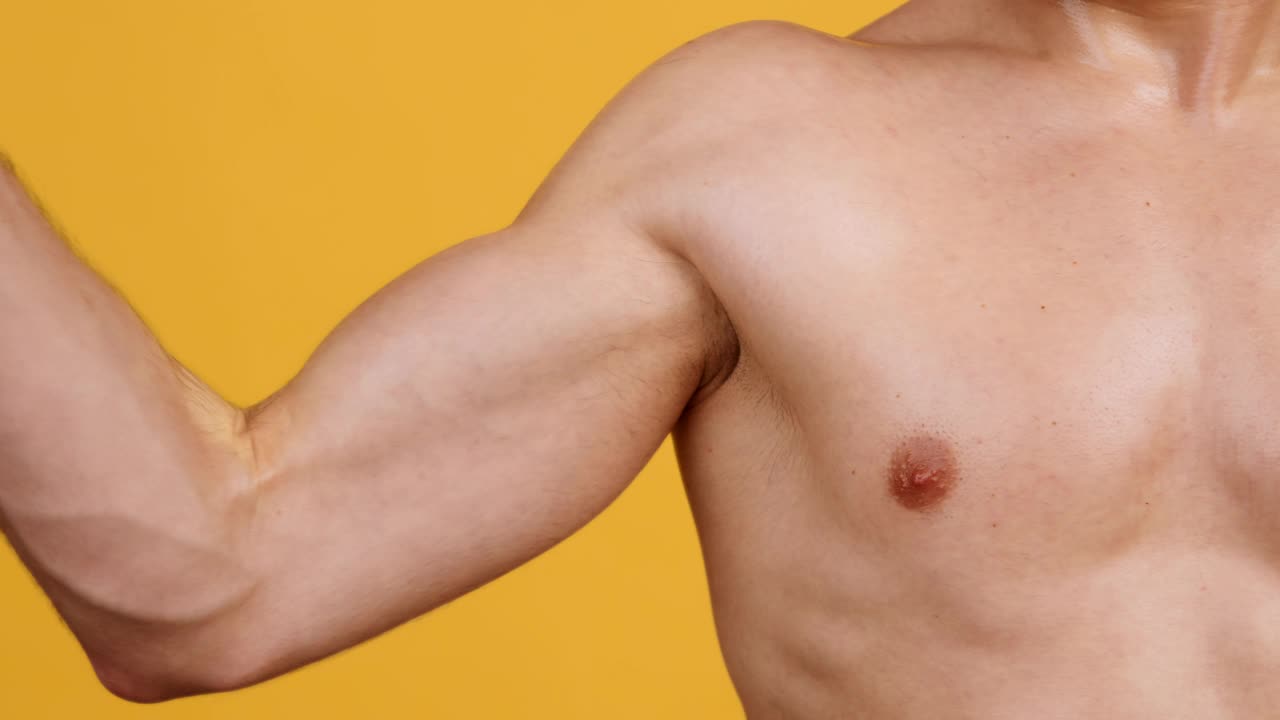 不知名的上身赤裸的运动员弯曲肌肉的二头肌，在橙色的背景下锻炼，慢动作视频下载