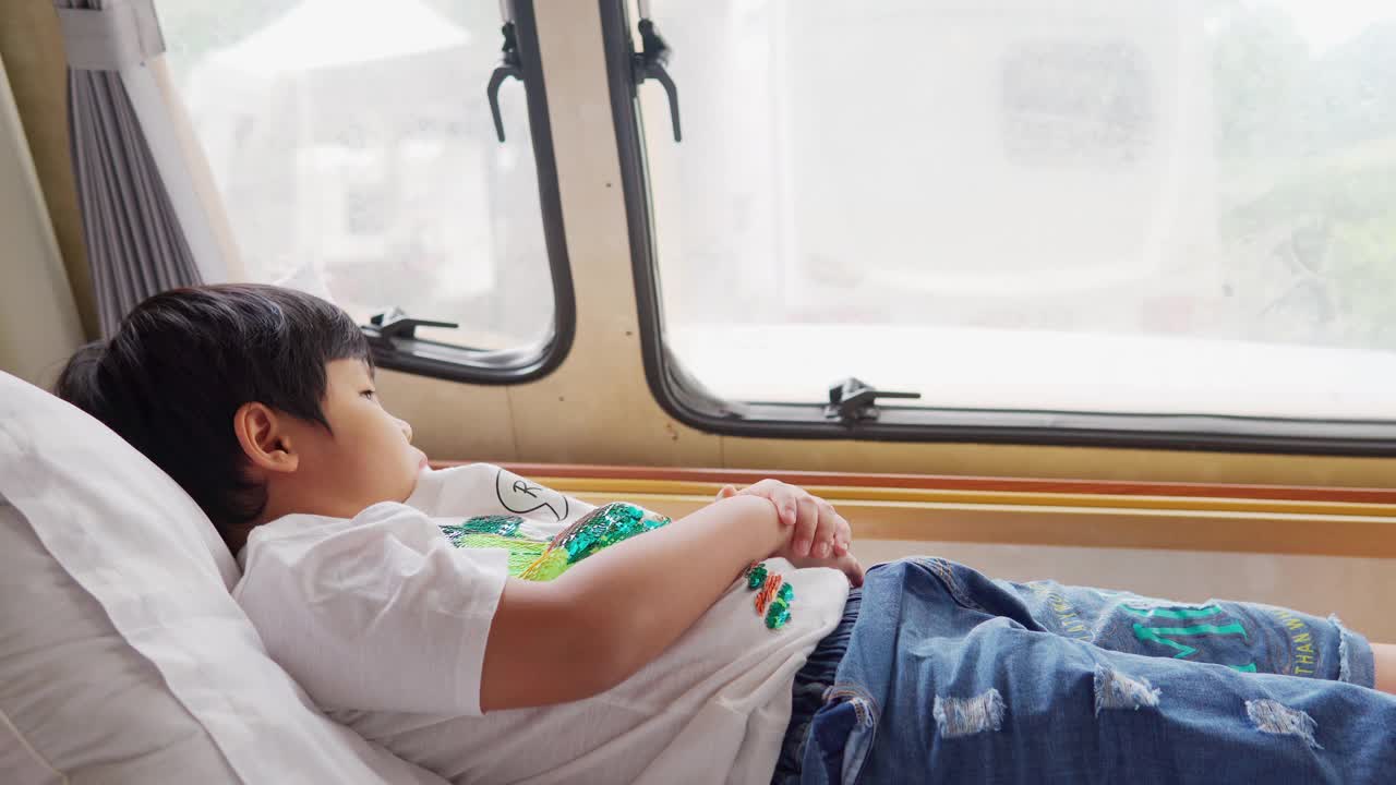 亚洲小男孩感觉放松在一辆野营车与窗外的景色在假日早上视频素材