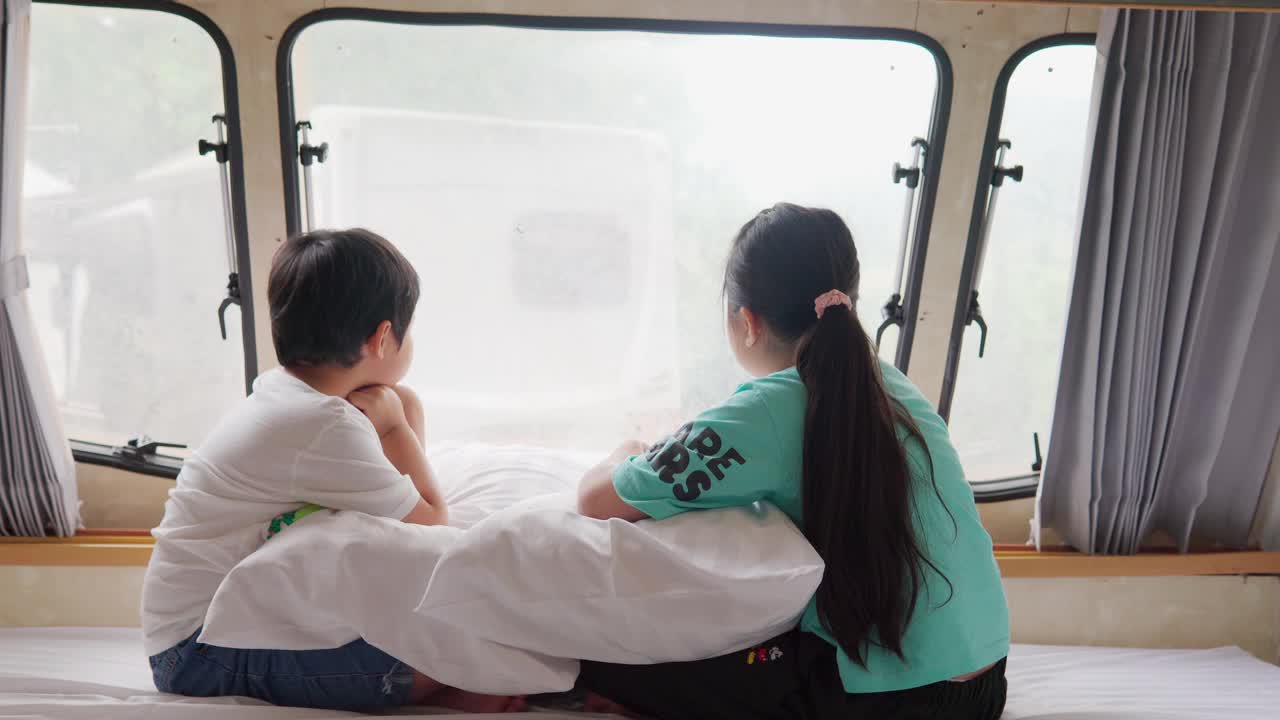 亚洲兄弟和姐妹感觉放松在一辆露营车与窗外的景色在假日早上视频素材