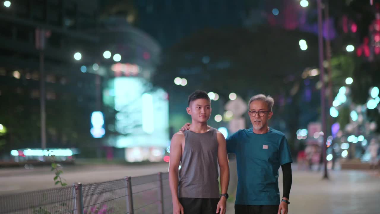 亚洲华人活跃的老人和他的儿子在晚上一起跑步锻炼后散步聊天城市视频下载