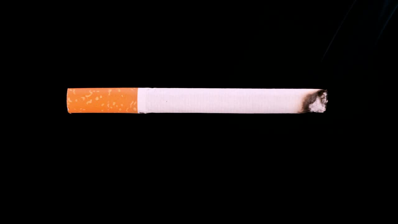 一根香烟燃烧的时间间隔视频，在黑色背景下阴燃。4 k决议。健康,成瘾概念。视频素材