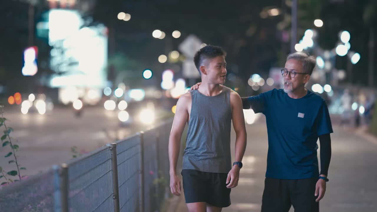 亚洲华人活跃的老人和他的儿子在晚上一起跑步锻炼后散步聊天城市视频素材