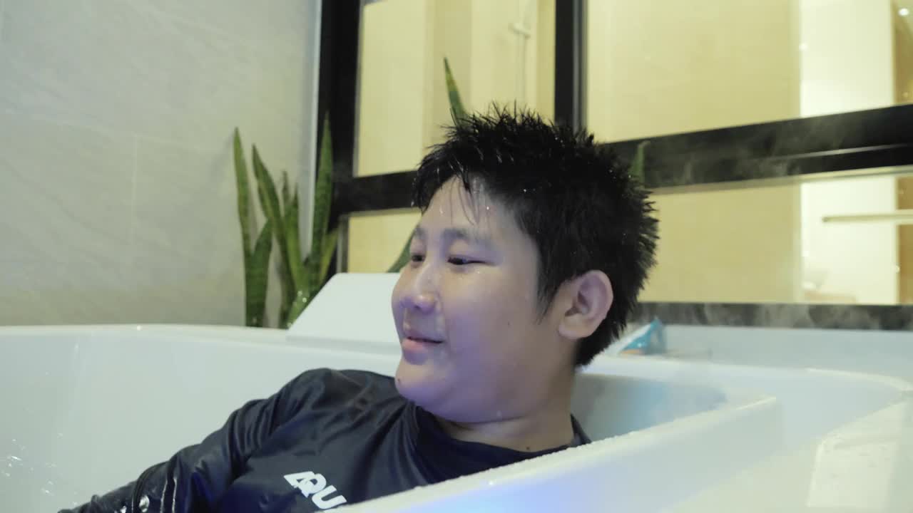 快乐的亚洲男孩有新的体验在酒店房间的热水浴缸在他的假期，生活方式的概念。视频下载
