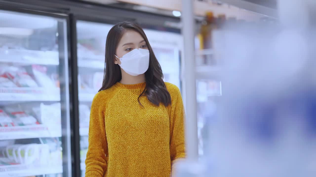 购物在新冠肺炎的传播，亚洲女性成年女性戴口罩保护手拉购物车选择购买消费品在百货商店货架上杂货新常态的生活方式视频素材