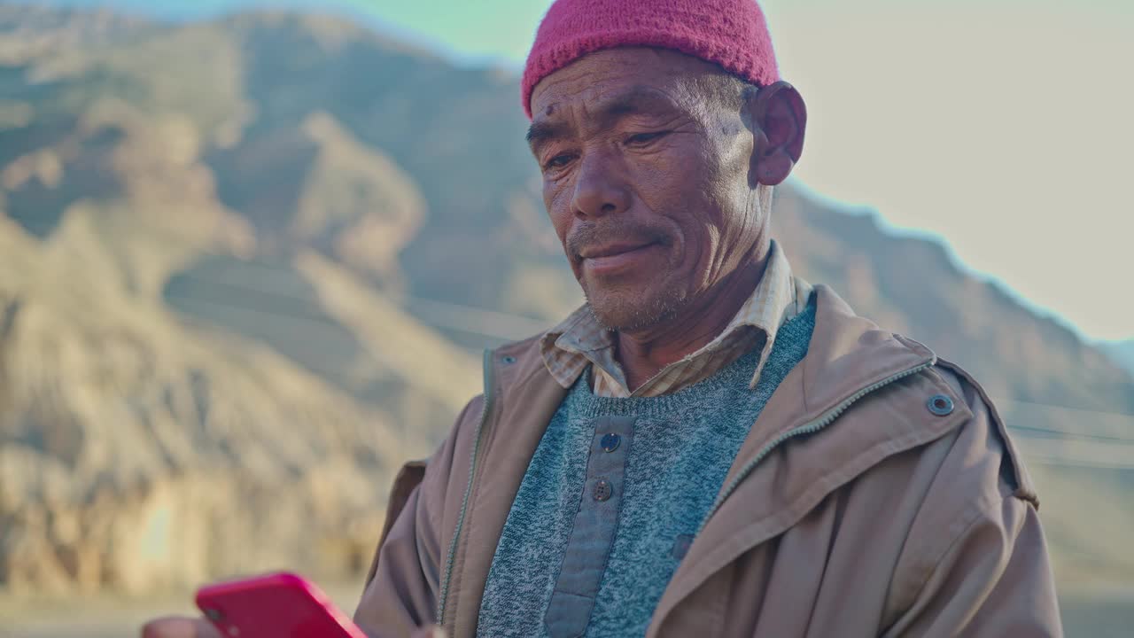 一个东亚老人站在贫瘠的土地上用智能手机视频下载