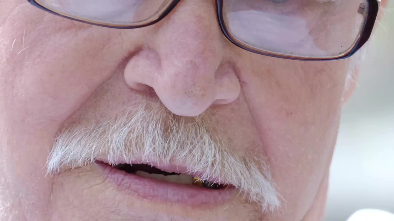 一位戴着眼镜、留着灰色胡子的老爷爷在说话，视频素材