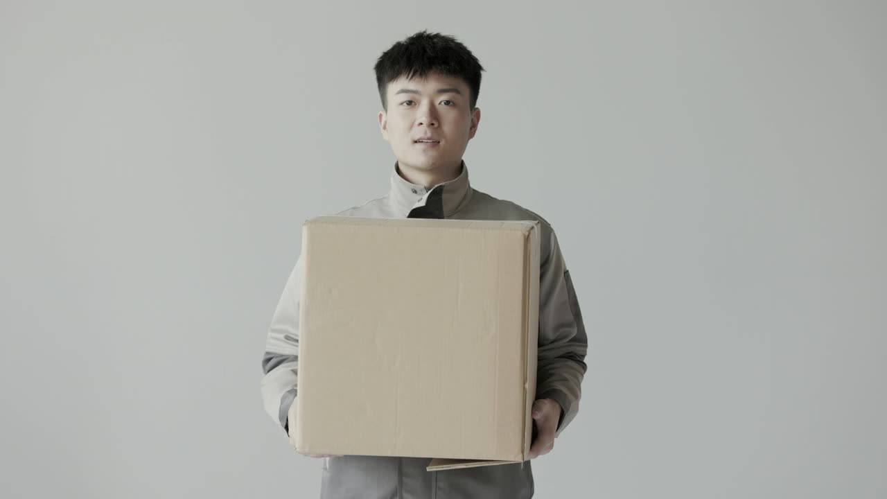 年轻的亚洲快递员穿着快递公司的制服，把快递箱递给了顾客视频购买