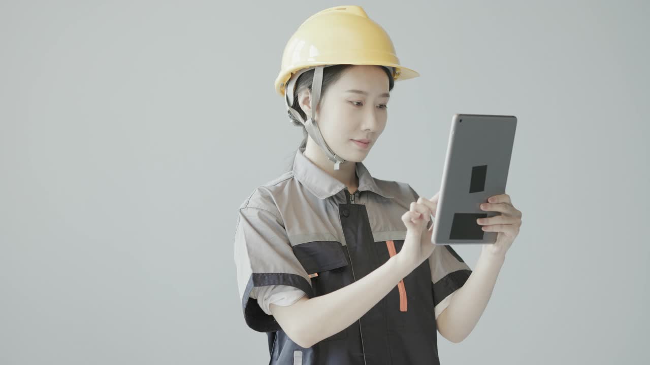 一名戴着黄色头盔的年轻漂亮的亚洲工人正在微笑着操作平板电脑视频下载