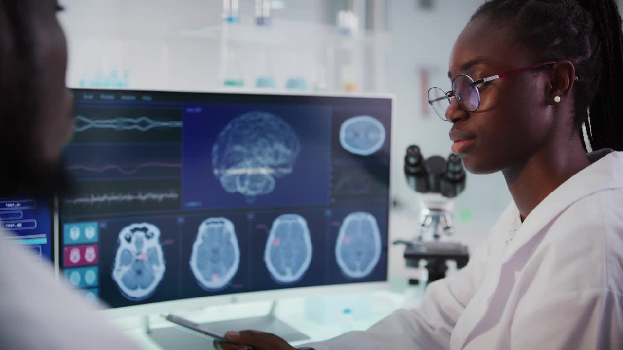 实验室设备和计算机。屏幕上的脑电波研究。非洲裔科学家讨论视频下载