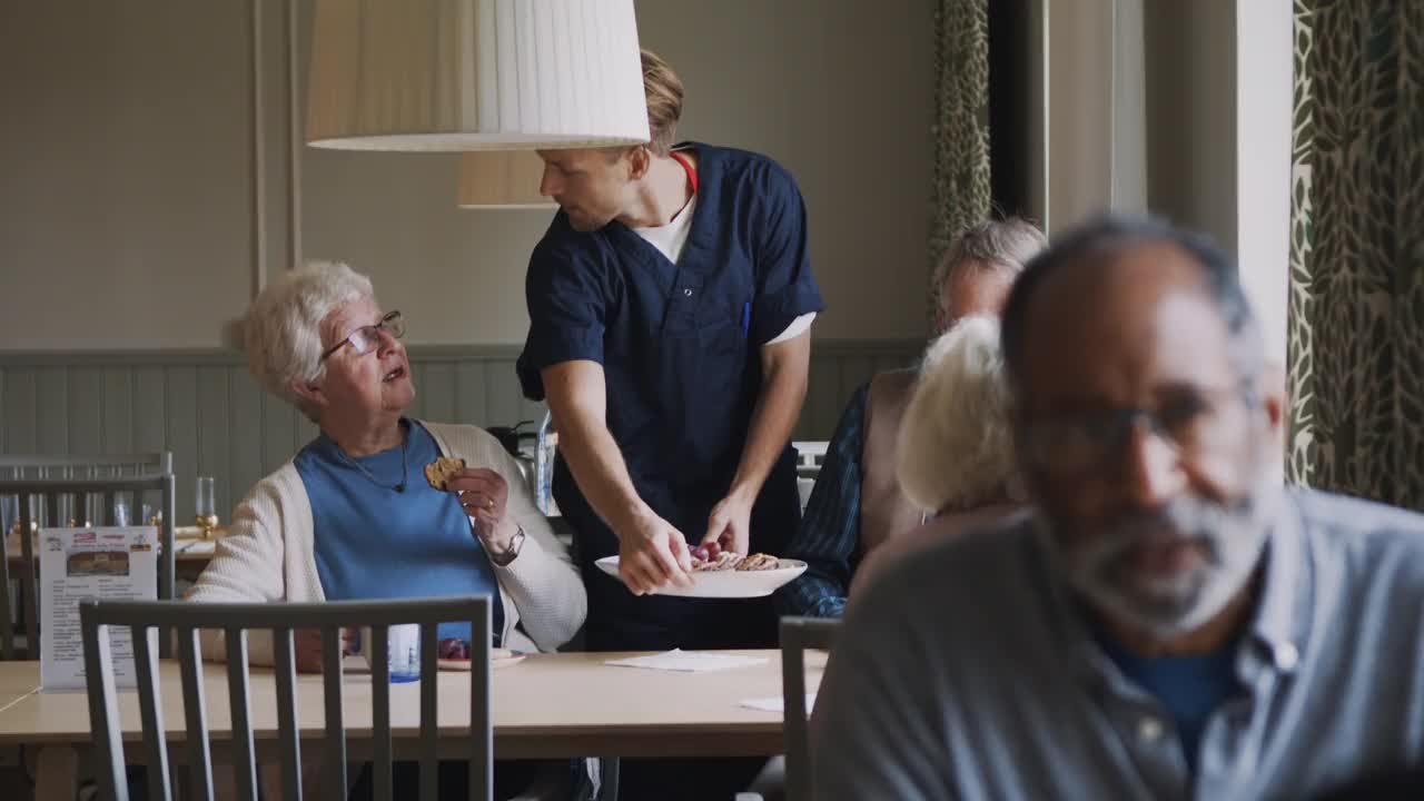 在退休之家的餐桌上，一位年长的妇女与为他们提供早餐的男性护理人员交谈视频素材