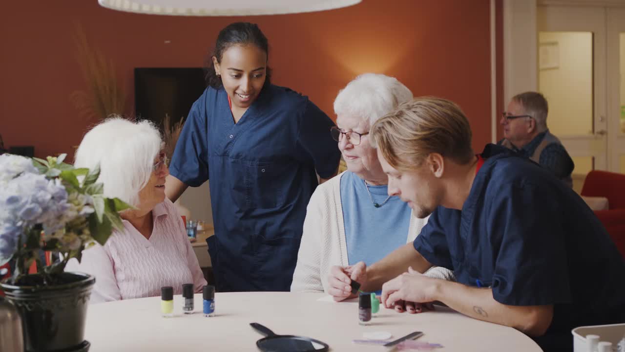 男医护人员在高级女士手上涂指甲油，而女护士在餐桌上与他们交谈视频素材