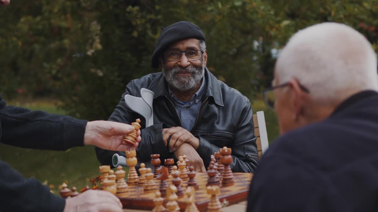 在公园里，一位面带微笑的老人坐在男性朋友旁边下棋视频素材