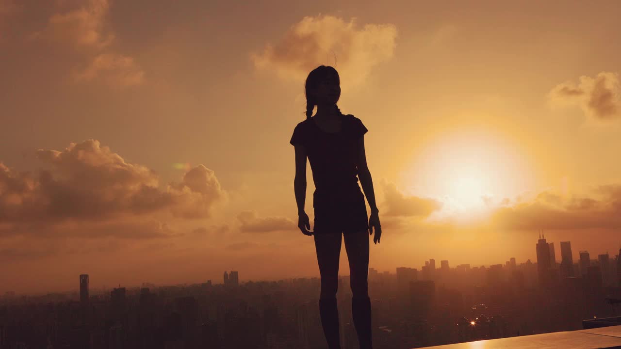 年轻快乐的女子在美丽的夕阳下跳舞，现代都市的背景视频素材