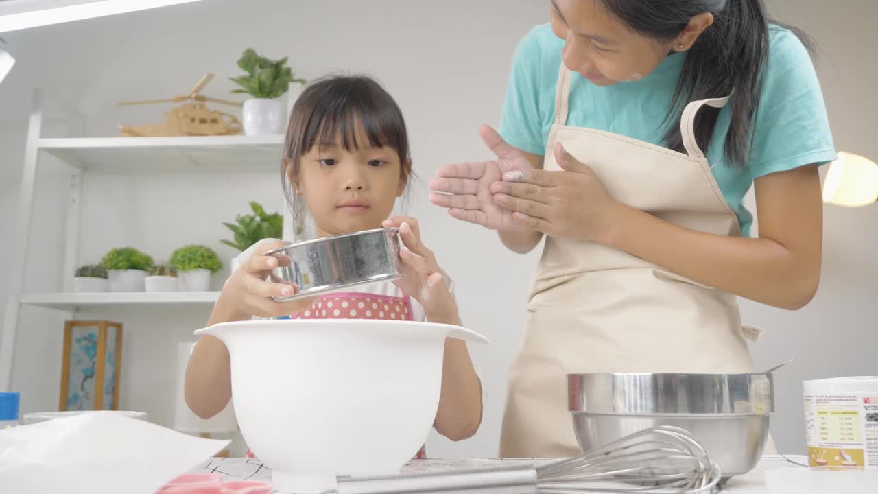 快乐的亚洲孩子在家里学习做饼干，女孩筛面粉到搅拌碗。视频素材