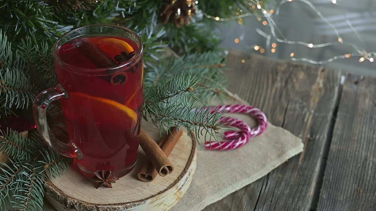 圣诞杯热热红酒与橙子，丁香，肉桂和茴芹附近的礼物和装饰。以圣诞彩灯为背景，温馨气氛，喜庆气氛。家庭时间，新年前夜。视频素材