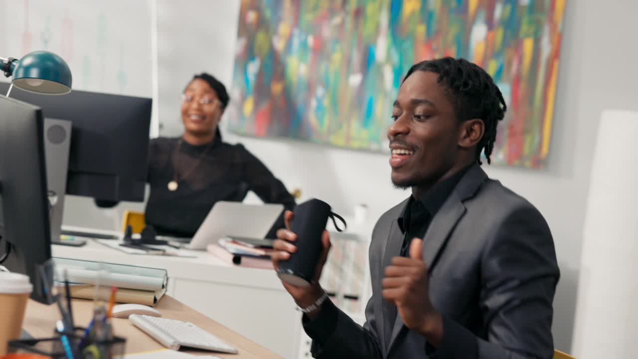 深色皮肤的同事坐在公司办公室的电脑前，跳舞，唱歌，为胜利而高兴，获得晋升，即将结束工作，良好的氛围，有趣视频素材