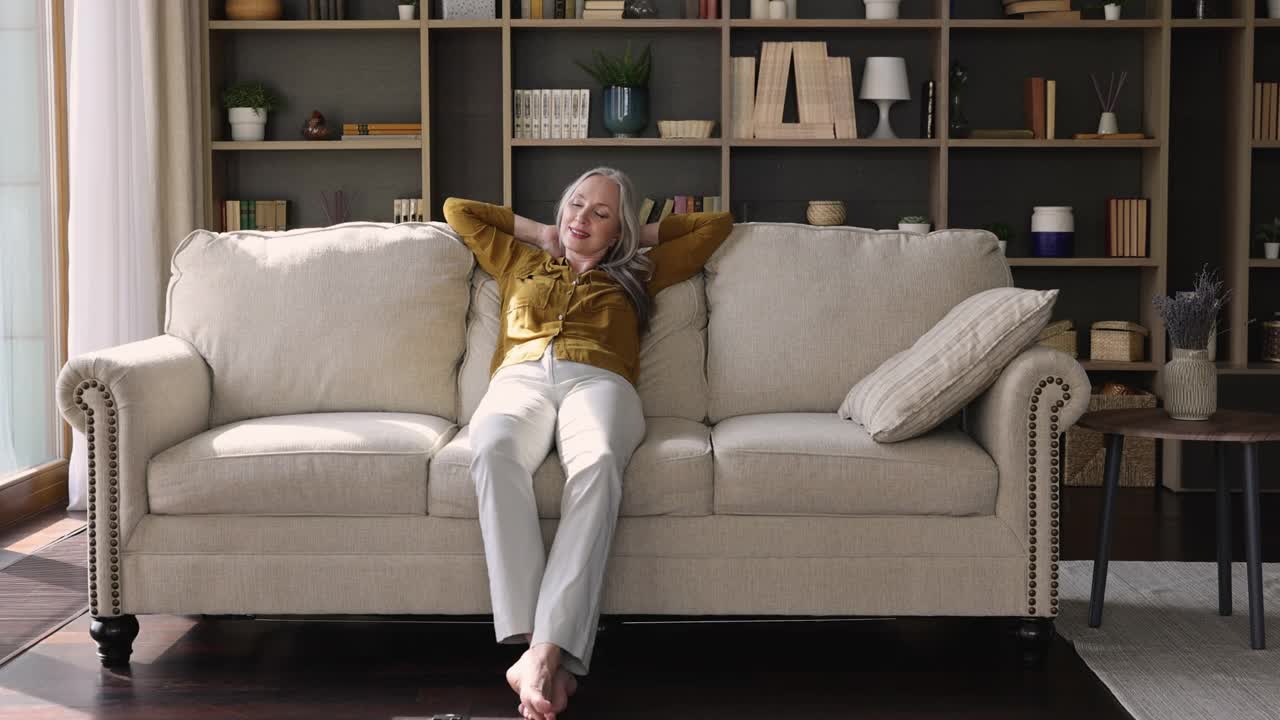 安详的老妇人把手放在脑后，在沙发上放松视频素材