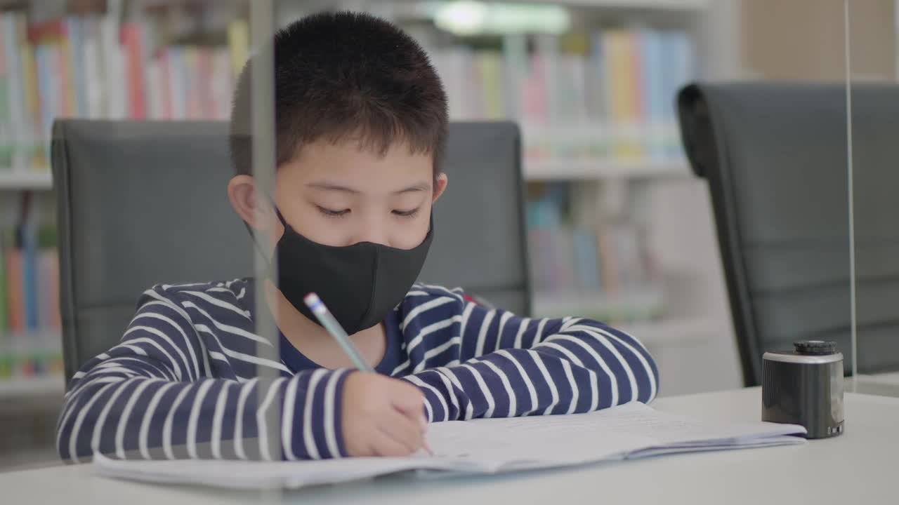 一个亚洲小男孩坐在图书馆里做作业，发呆，无聊，不想工作视频下载